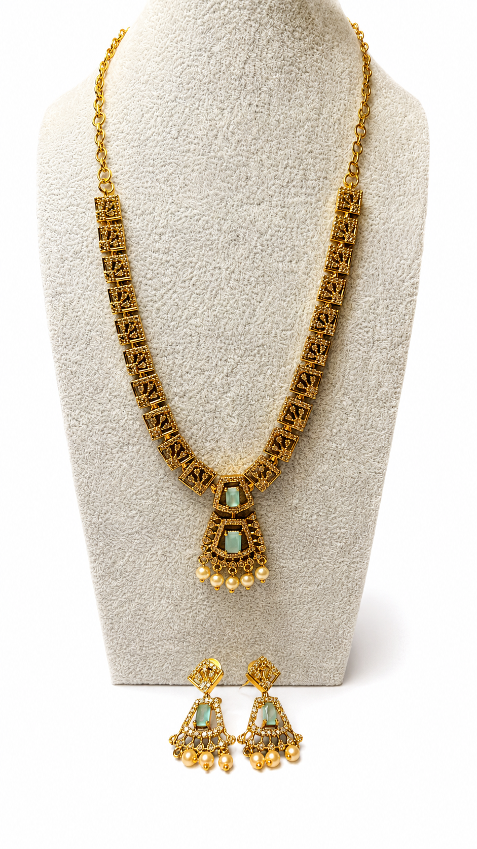 Gold-toned traditional jewelry set featuring a long chain necklace and matching drop earrings, displayed on a textured cream jewelry bust against a white background.