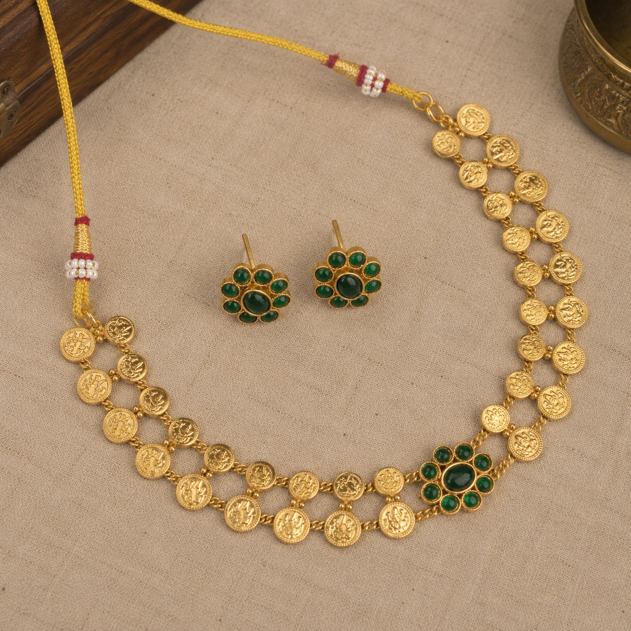Gold-toned traditional jewelry set featuring a necklace and matching earrings with green stone floral accents, displayed on a beige fabric surface.