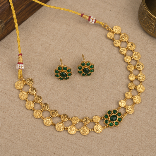 Gold-toned traditional jewelry set featuring a necklace and matching earrings with green stone floral accents, displayed on a beige fabric surface.