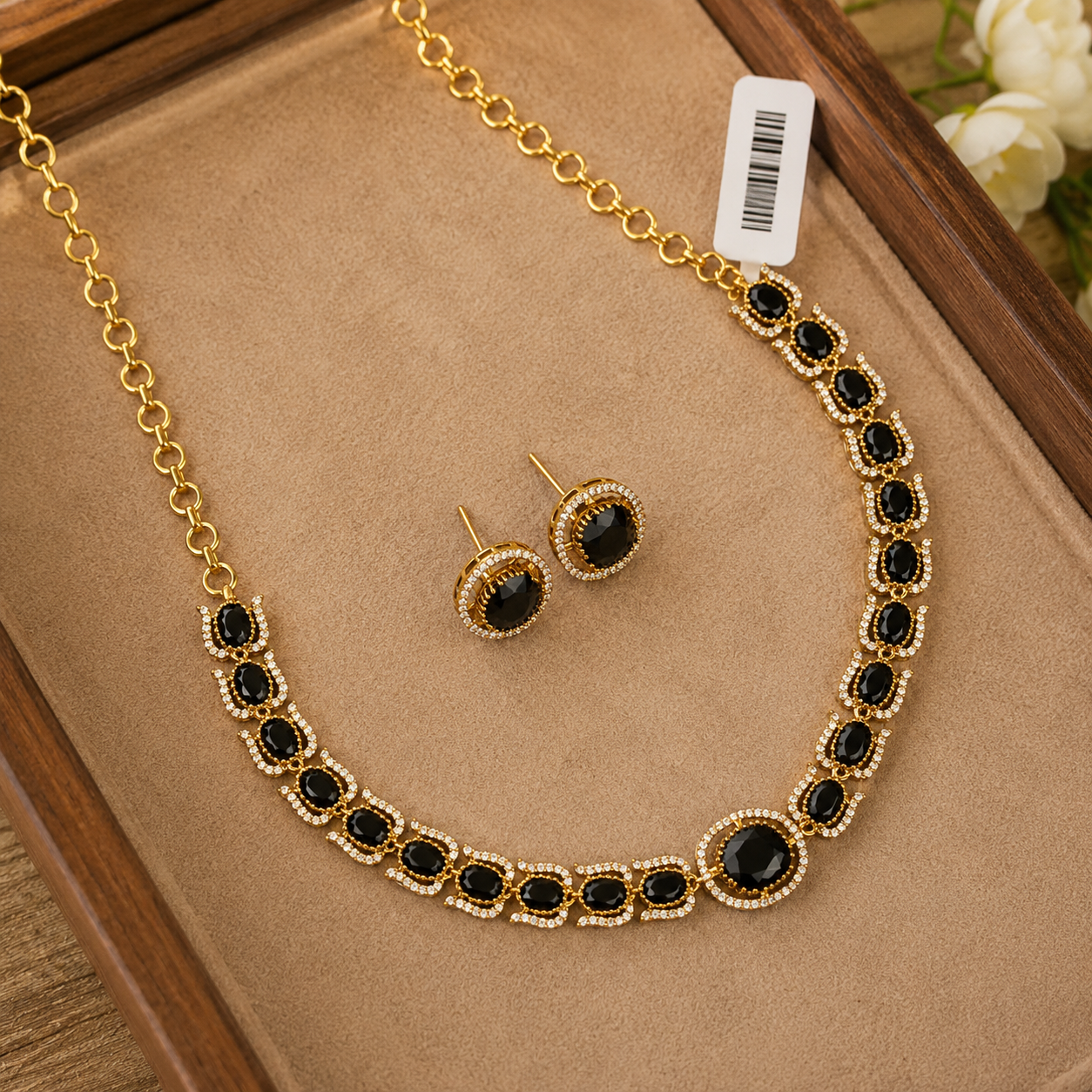 Gold-tone necklace and matching stud earrings set with oval black stones and small clear crystal-like accents, displayed on a tan jewelry tray inside a wooden box.