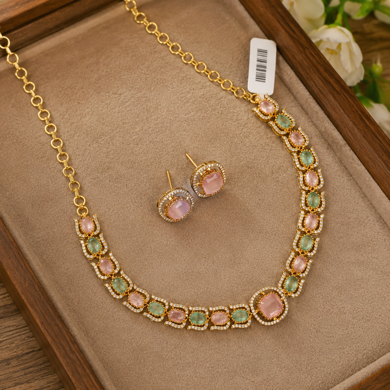 Gold-tone necklace and matching stud earrings set with pink and green stones, displayed on a beige jewelry tray.