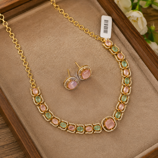 Gold-tone necklace and matching stud earrings set with pink and green stones, displayed on a beige jewelry tray.