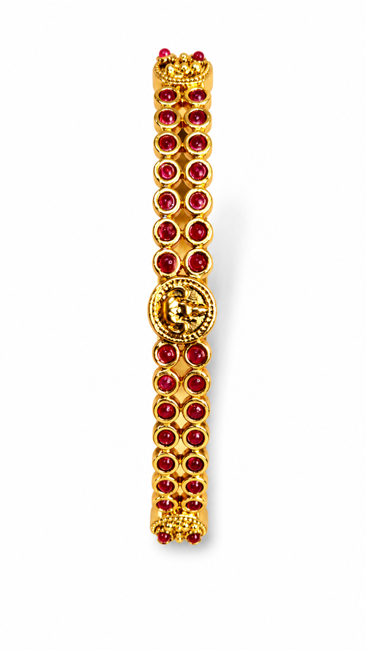 A gold-plated bracelet featuring rows of round red gemstones and a central decorative medallion, shown on a plain white background.