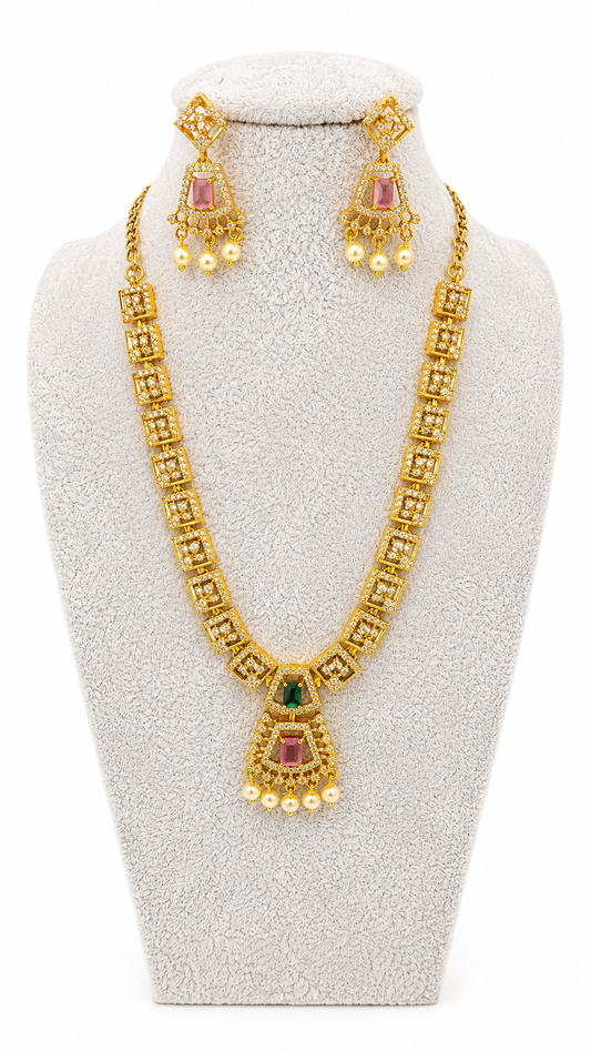 Gold-toned traditional jewelry set displayed on a textured white jewelry bust, including a necklace with a teardrop pendant and matching drop earrings, featuring pink stones, green stones, and small pearl-like beads.