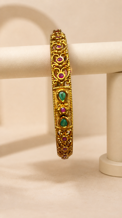 Antique ruby and emerald filigree bangle from Belumiee, showcasing intricate metalwork and vibrant gemstone details.