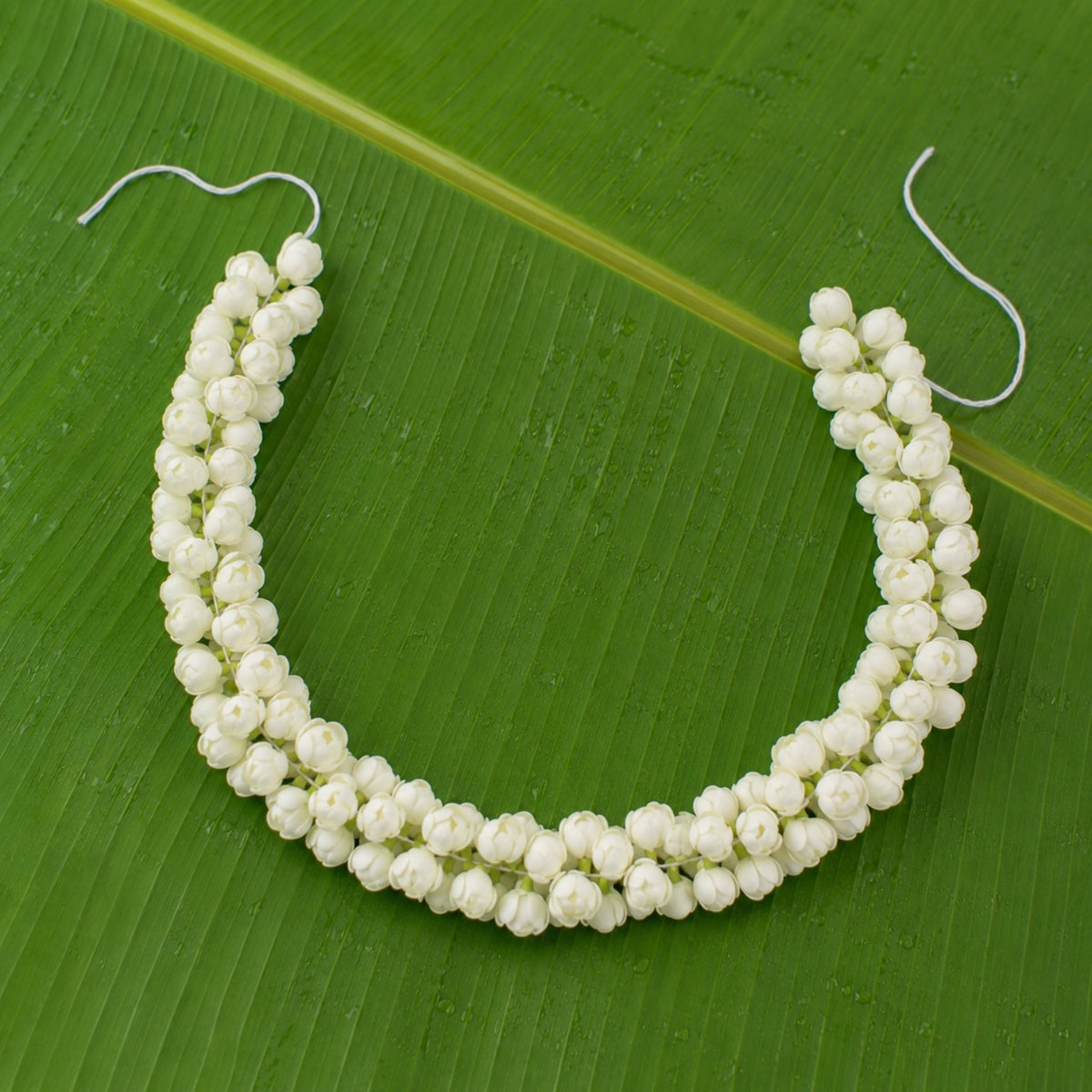 Double-layer artificial jasmine hair garland arranged on a green banana leaf