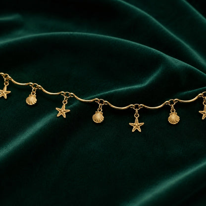Close-up of alternating starfish and seashell charms on a gold-tone wave-link hip chain
