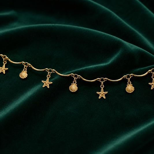 Close-up of alternating starfish and seashell charms on a gold-tone wave-link hip chain