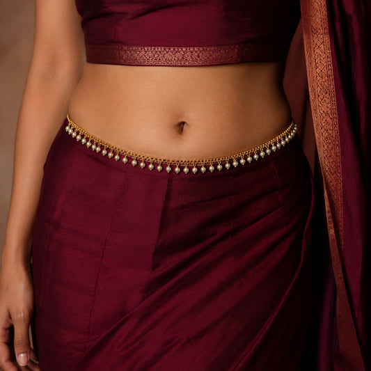Model wearing gold-tone white pearl fringe hip chain with burgundy saree