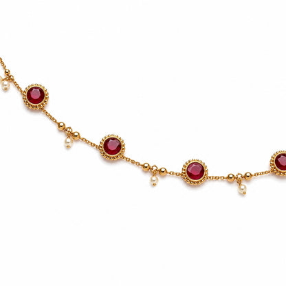 Close-up of gold-tone hip chain with round ruby-coloured stones, gold beads and pearl drops